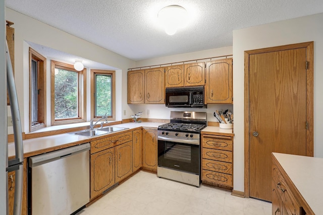 kitchen featuring stainless steel appliances, a sink, light countertops, a textured ceiling, and brown cabinets