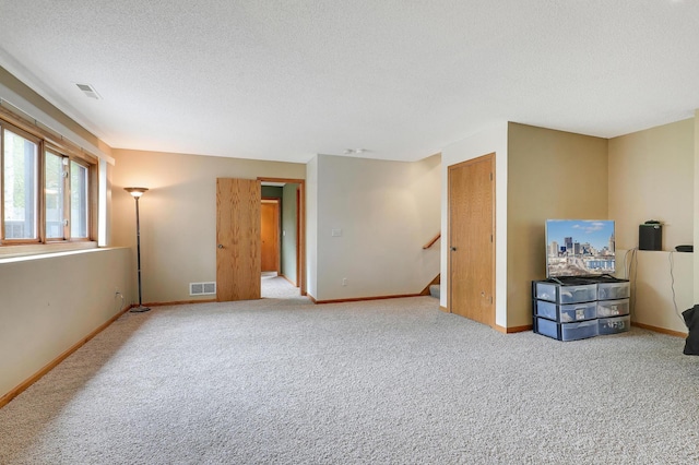unfurnished living room with a textured ceiling, baseboards, carpet flooring, and stairway