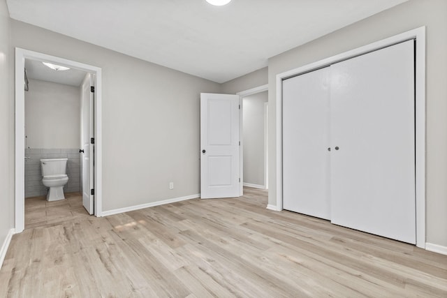 228 16th Ave SW, New Brighton, MN 55112 - unfurnished bedroom featuring light wood-type flooring, connected bathroom, a closet, baseboards, and tile walls