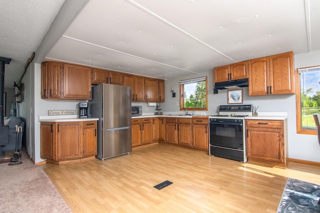 692 Round Lake Ln, Georgetown Twp, WI 54853 - kitchen featuring gas range oven, freestanding refrigerator, light wood-style floors, brown cabinetry, and a wood stove