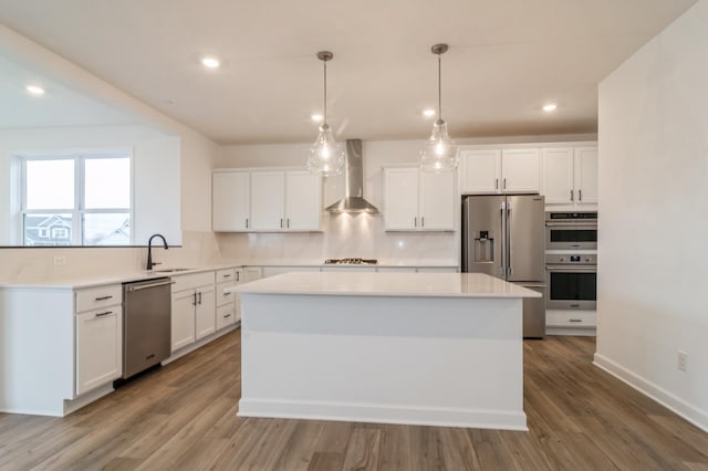 kitchen with stainless steel appliances, wall chimney exhaust hood, a center island, white cabinetry, and a sink