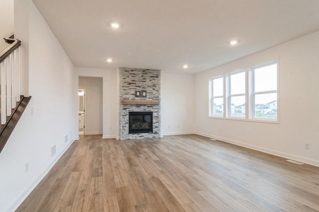 unfurnished living room featuring light wood finished floors, stairs, a fireplace, recessed lighting, and baseboards