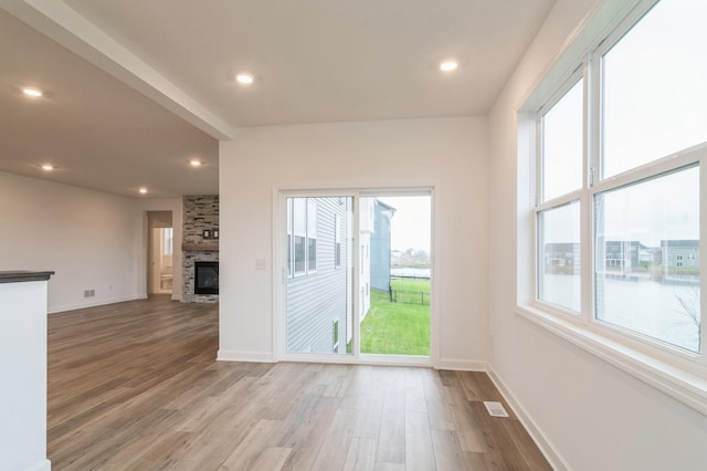 unfurnished living room with wood finished floors, baseboards, a stone fireplace, and recessed lighting