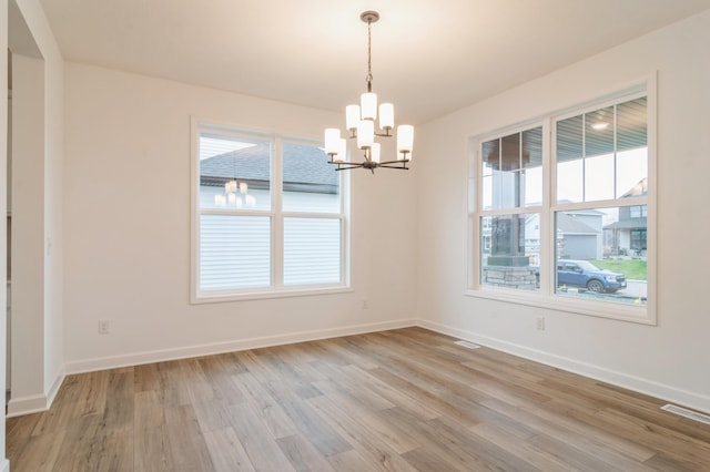 empty room featuring a chandelier, healthy amount of natural light, and light wood-style flooring