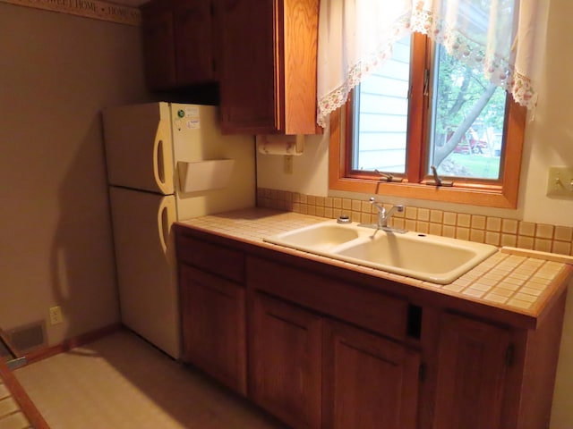 114 2nd St S, Truman, MN 56088 - kitchen featuring a sink, tile countertops, freestanding refrigerator, and brown cabinetry