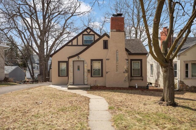 1750 Sims Ave, Saint Paul, MN 55106 - tudor-style house featuring stucco siding, a chimney, a front yard, and roof with shingles