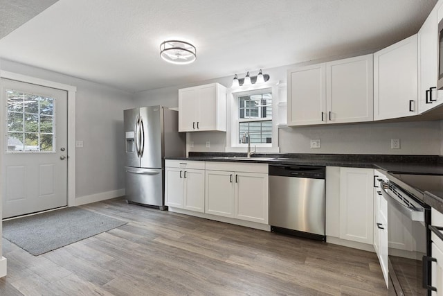806 4th St, Marshall, MN 56258 - kitchen featuring stainless steel appliances, a sink, light wood-style flooring, white cabinetry, and dark countertops