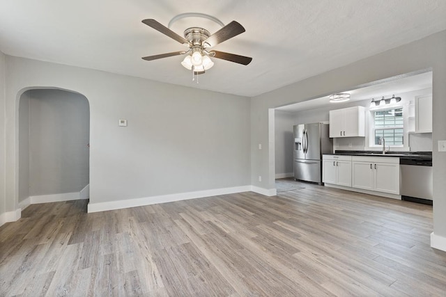 806 4th St, Marshall, MN 56258 - unfurnished living room with a sink, light wood finished floors, a ceiling fan, arched walkways, and baseboards