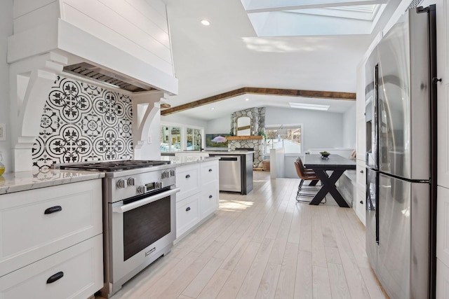 168 1st St, Excelsior, MN 55331 - kitchen with appliances with stainless steel finishes, a skylight, white cabinets, light wood-style floors, and light stone countertops