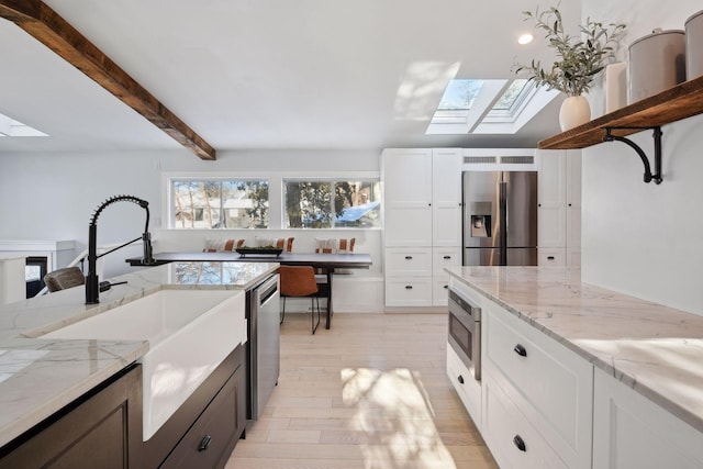 168 1st St, Excelsior, MN 55331 - kitchen featuring a skylight, appliances with stainless steel finishes, a sink, white cabinetry, and beam ceiling
