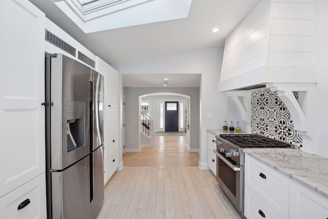 168 1st St, Excelsior, MN 55331 - kitchen with stainless steel appliances, arched walkways, a skylight, white cabinets, and lofted ceiling