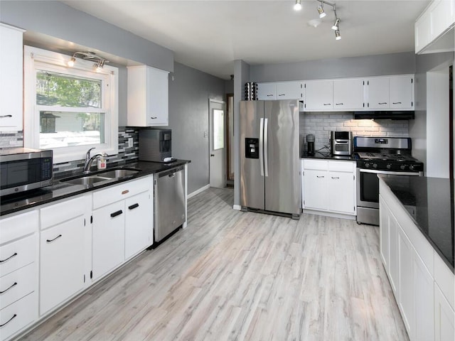 kitchen with appliances with stainless steel finishes, a sink, tasteful backsplash, and light wood-type flooring