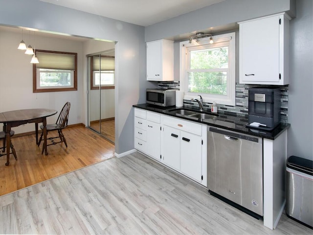 kitchen featuring stainless steel appliances, a sink, dark countertops, light wood-style floors, and white cabinets