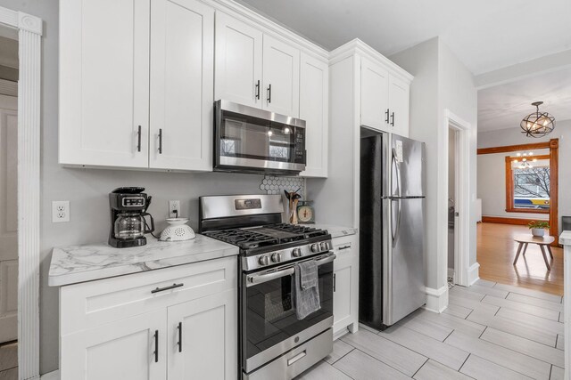 2744 Stevens Ave, Minneapolis, MN 55408 - kitchen with appliances with stainless steel finishes, a chandelier, white cabinetry, baseboards, and light stone countertops