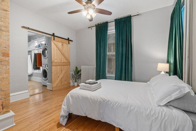 2744 Stevens Ave, Minneapolis, MN 55408 - bedroom with stacked washer / dryer, radiator heating unit, a barn door, wood finished floors, and ceiling fan