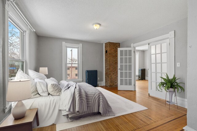 2744 Stevens Ave, Minneapolis, MN 55408 - bedroom featuring radiator, french doors, a textured ceiling, multiple windows, and wood-type flooring
