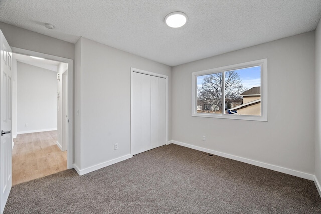 unfurnished bedroom with carpet, a closet, baseboards, and a textured ceiling