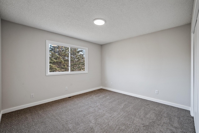 spare room with dark colored carpet, a textured ceiling, and baseboards