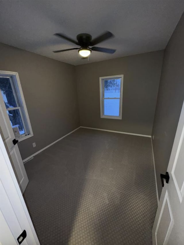 unfurnished room with a ceiling fan, baseboards, and dark colored carpet