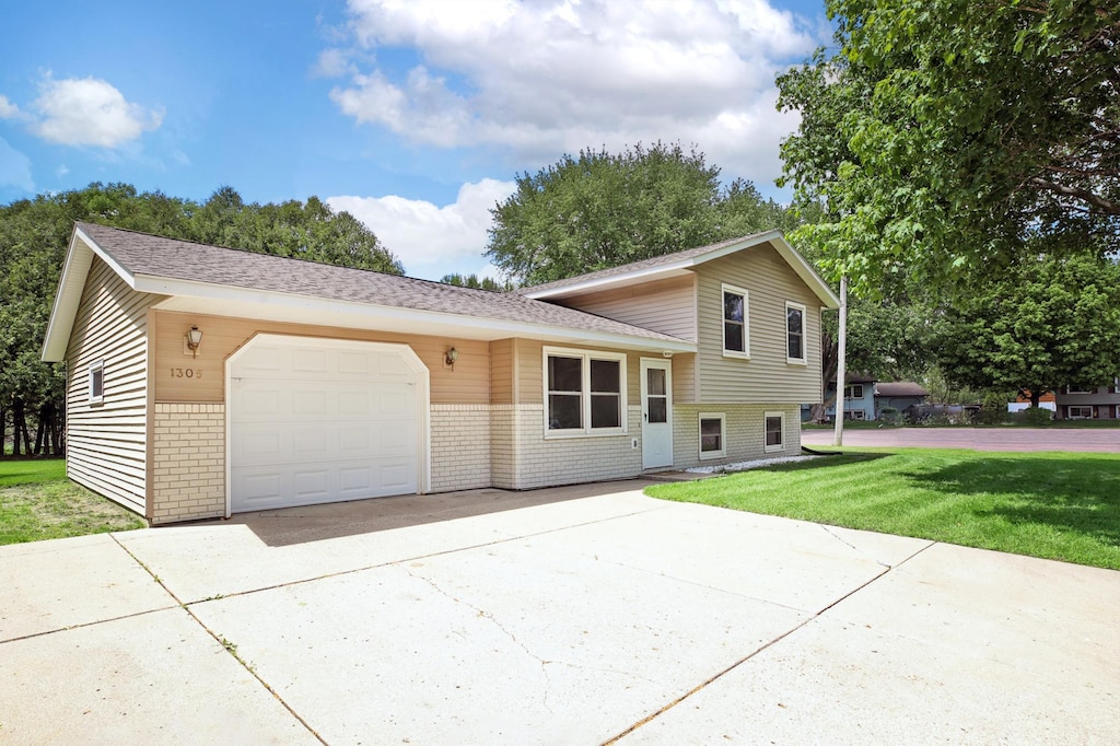 1305 5th St NW, Waseca, MN 56093 - tri-level home featuring brick siding, driveway, an attached garage, a front yard, and roof with shingles