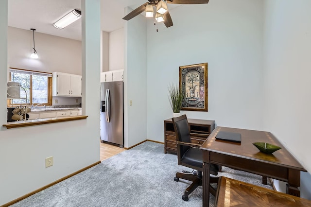office featuring light colored carpet, a towering ceiling, ceiling fan, and baseboards