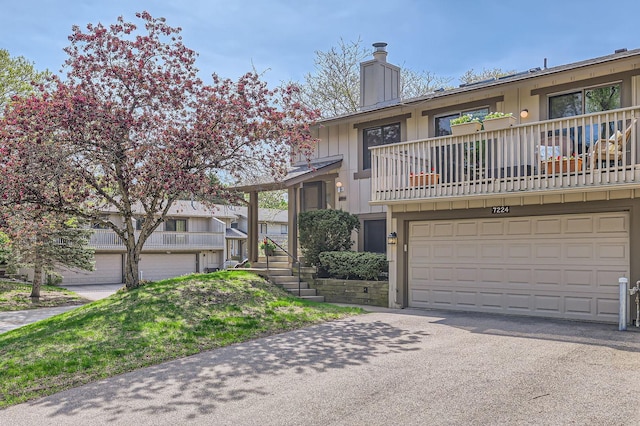 view of property featuring a balcony, a chimney, a garage, and driveway