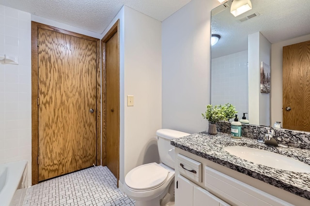 bathroom with a textured ceiling, toilet, vanity, and a bath