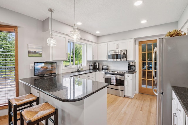 4650 Cottonwood Ln N, Plymouth, MN 55442 - kitchen with stainless steel appliances, a peninsula, white cabinets, light wood-style floors, and a kitchen breakfast bar