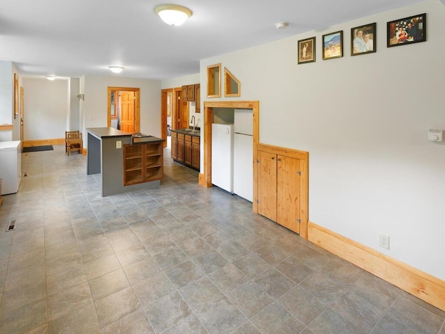 601 Kingsway Dr, Le Sueur, MN 56058 - kitchen featuring baseboards, dark countertops, a kitchen island, a sink, and brown cabinetry