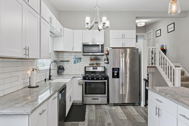 kitchen featuring stainless steel appliances, light wood-type flooring, a sink, white cabinetry, and tasteful backsplash