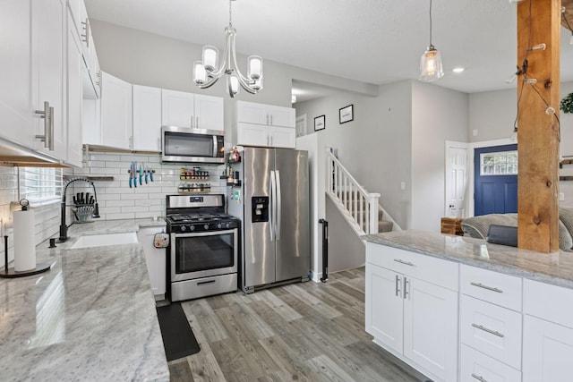 kitchen featuring stainless steel appliances, decorative backsplash, a sink, white cabinetry, and a chandelier