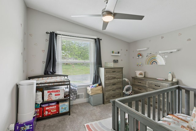 carpeted bedroom with lofted ceiling, a crib, and a ceiling fan