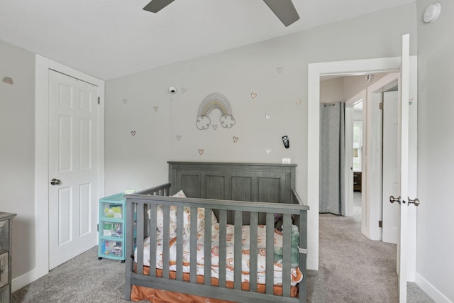 bedroom featuring carpet flooring, a crib, baseboards, and a ceiling fan