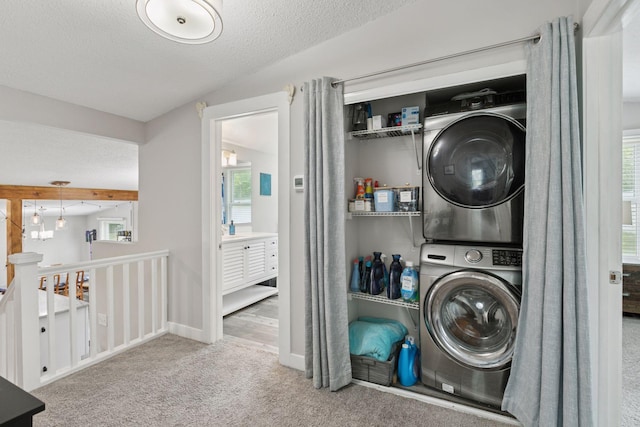 laundry room with stacked washer / dryer, carpet floors, a textured ceiling, healthy amount of natural light, and baseboards