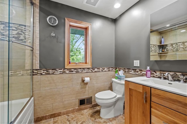 2511 Carver Ave E, Maplewood, MN 55119 - bathroom with toilet, tile walls, vanity, shower / bath combination with glass door, and a wainscoted wall