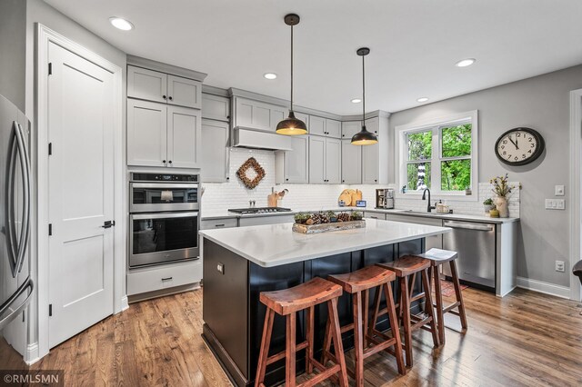 7023 61st St S, Cottage Grove, MN 55016 - kitchen with appliances with stainless steel finishes, a sink, backsplash, a kitchen bar, and wood finished floors