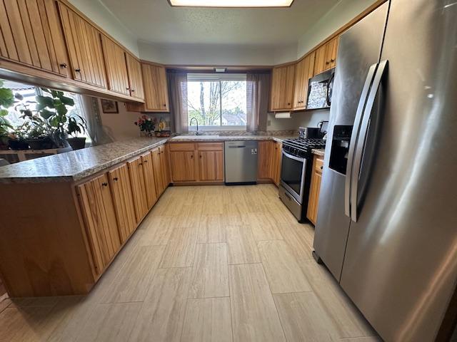 22 Cottonwood Ct, Babbitt, MN 55706 - kitchen with stainless steel appliances, a sink, brown cabinetry, and light wood-style flooring