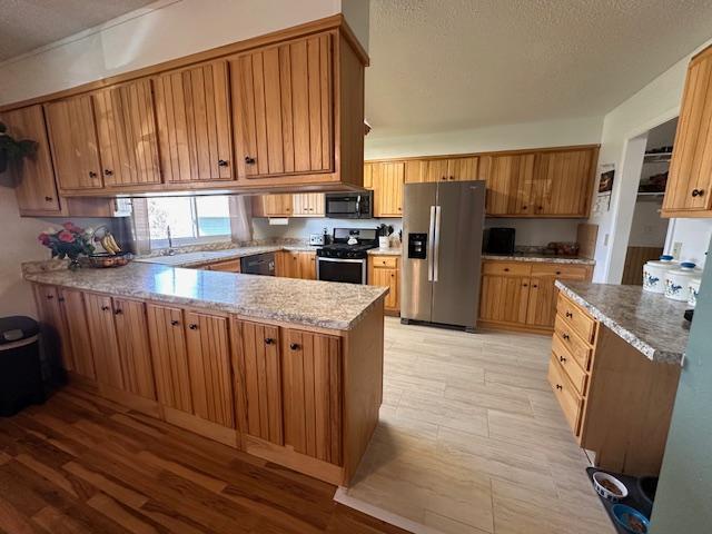22 Cottonwood Ct, Babbitt, MN 55706 - kitchen featuring black appliances, a peninsula, brown cabinets, a textured ceiling, and light wood-style flooring
