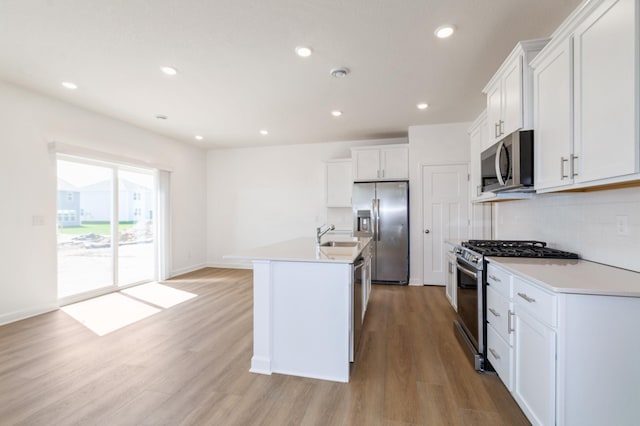 kitchen with appliances with stainless steel finishes, light wood finished floors, a kitchen island with sink, white cabinetry, and recessed lighting