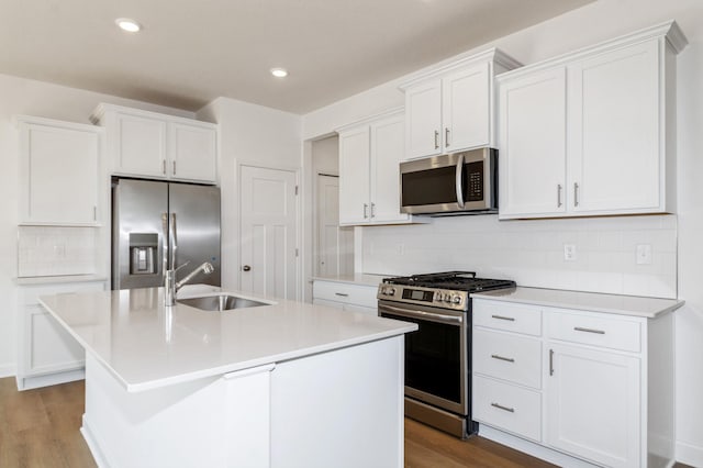 kitchen with appliances with stainless steel finishes, a sink, wood finished floors, a kitchen island with sink, and recessed lighting