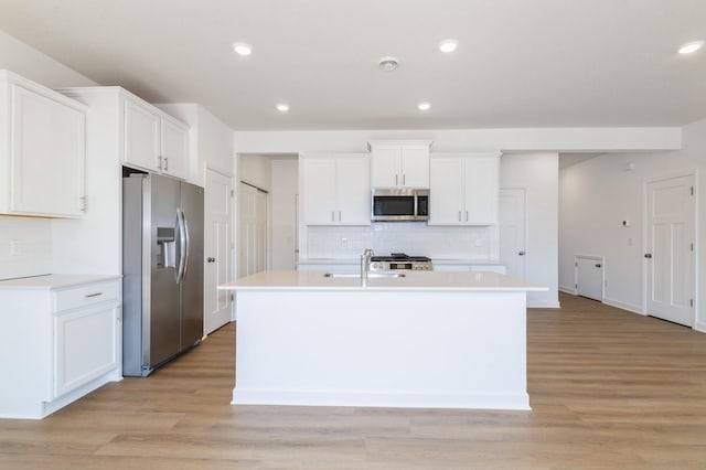 kitchen featuring stainless steel appliances, a sink, tasteful backsplash, light wood-style flooring, and a kitchen island with sink
