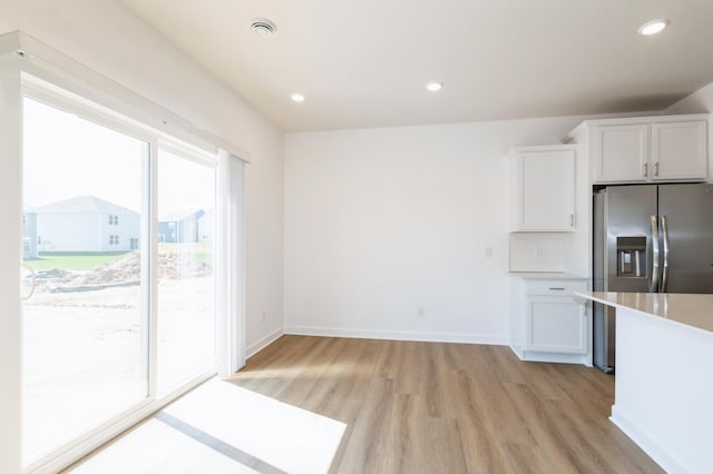 kitchen with light wood finished floors, white cabinetry, light countertops, stainless steel refrigerator with ice dispenser, and recessed lighting