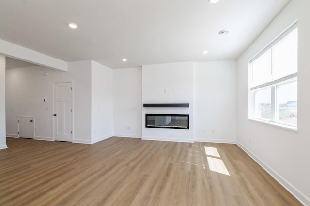 unfurnished living room with a glass covered fireplace, light wood-style floors, recessed lighting, and baseboards