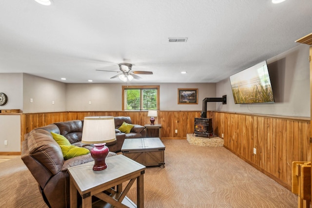 106 Prairie Grass Dr, Osceola, WI 54020 - living area featuring a wood stove, wooden walls, a wainscoted wall, a ceiling fan, and light colored carpet
