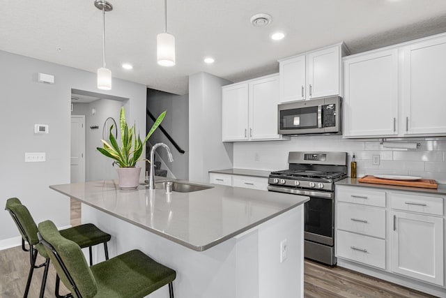 7243 Fall Dr, Lino Lakes, MN 55038 - kitchen featuring stainless steel appliances, wood finished floors, decorative backsplash, a kitchen bar, and white cabinets