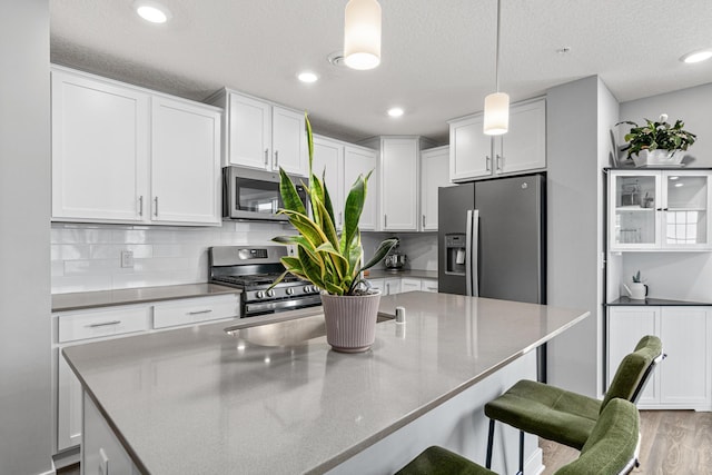 7243 Fall Dr, Lino Lakes, MN 55038 - kitchen featuring stainless steel appliances, white cabinetry, light wood finished floors, a kitchen breakfast bar, and hanging light fixtures