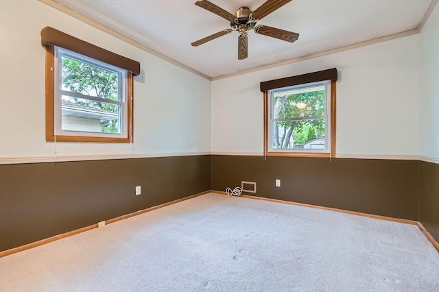 empty room featuring healthy amount of natural light, carpet, crown molding, a ceiling fan, and baseboards