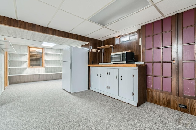 kitchen with stainless steel microwave, freestanding refrigerator, wooden walls, and carpet flooring