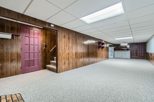 finished basement with wood walls, carpet flooring, stairway, and a paneled ceiling