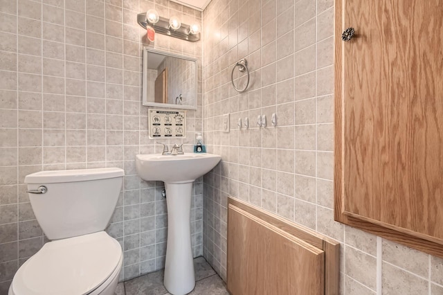 half bath with tile walls, toilet, and a sink